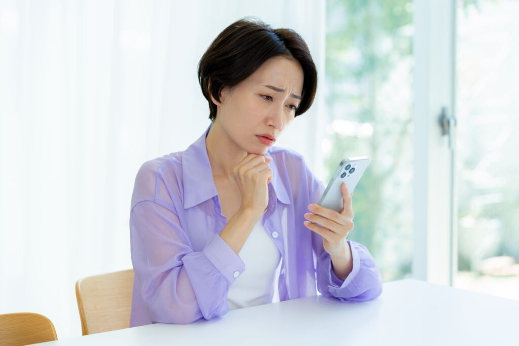 スマートフォンを見ながら不安そうに悩む女性