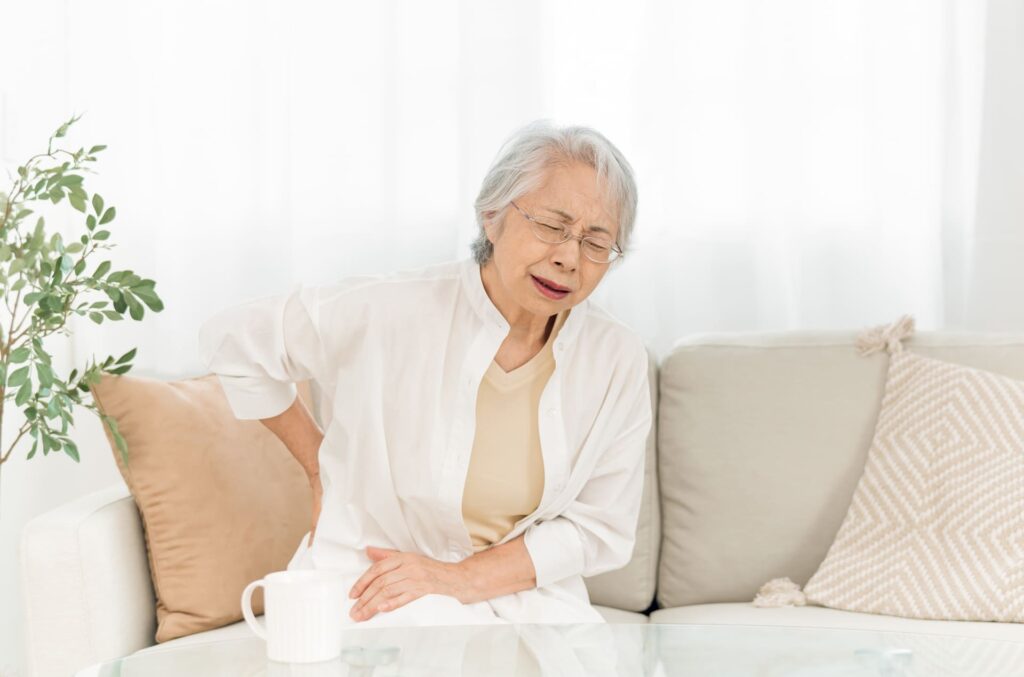 骨粗しょう症で腰を痛めている中年女性のイメージ写真。骨の健康と歯の関係を表現。