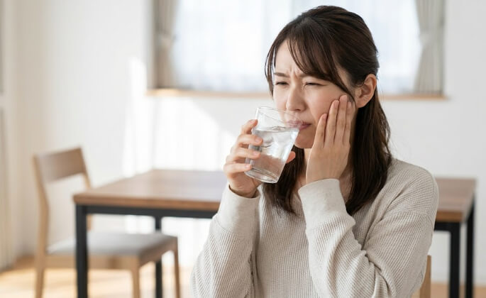冷たい水を飲んで、頬を抑えてしみる痛みに顔をしかめる日本人女性。