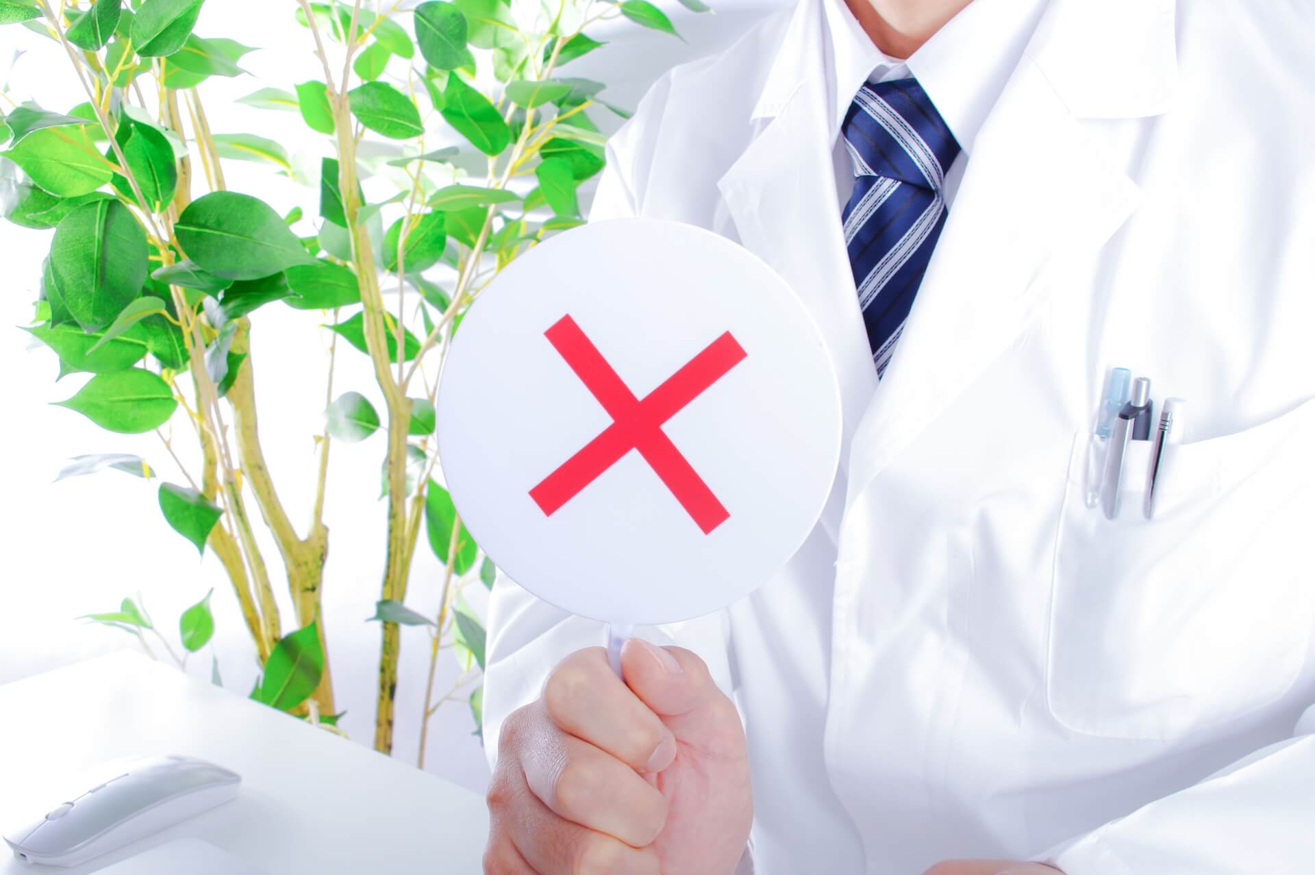 通常の虫歯や歯周病でのインプラント治療には公的保険が使えないことをバツ印で伝える歯科医師の様子