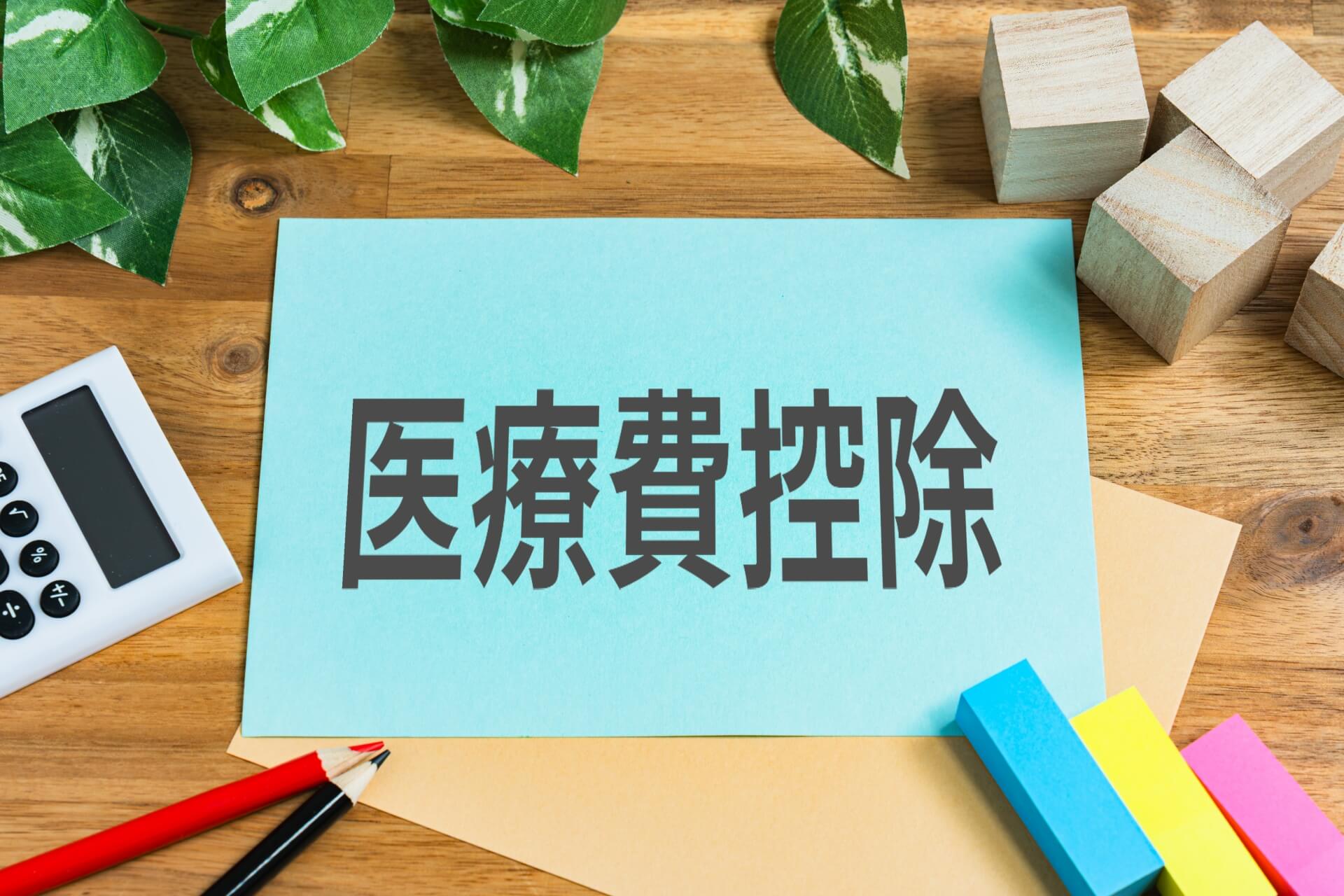 木製デスクの上に置かれた、「医療費控除」と書かれた青い紙と電卓