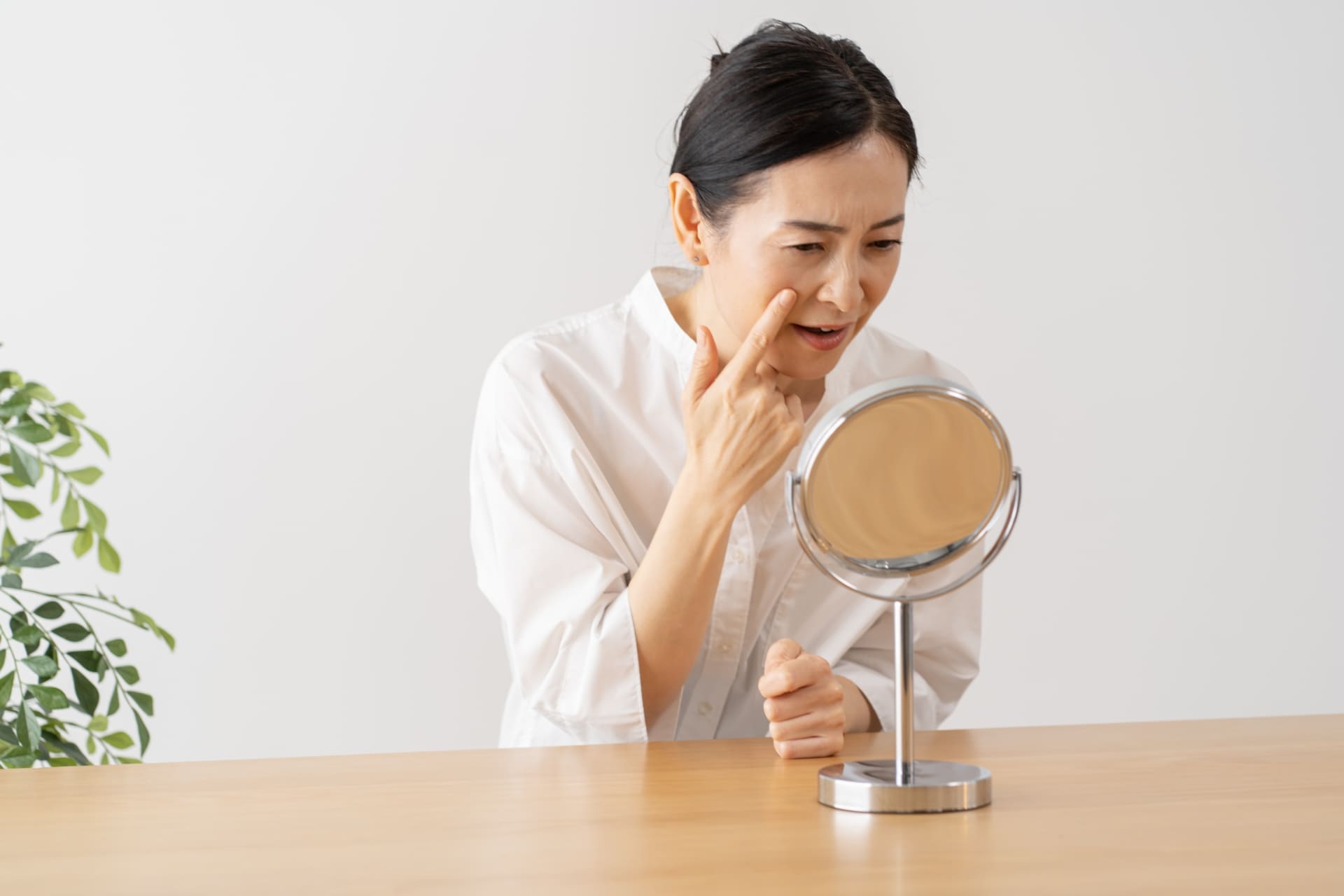 ほうれい線を気にして鏡を見る女性の写真