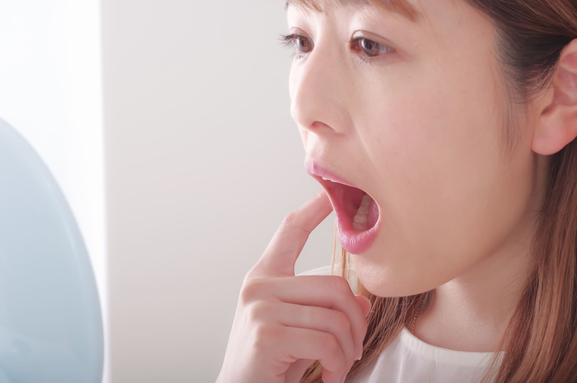 鏡で口の中を確認する女性の写真(歯茎下がりのセルフチェックイメージ)