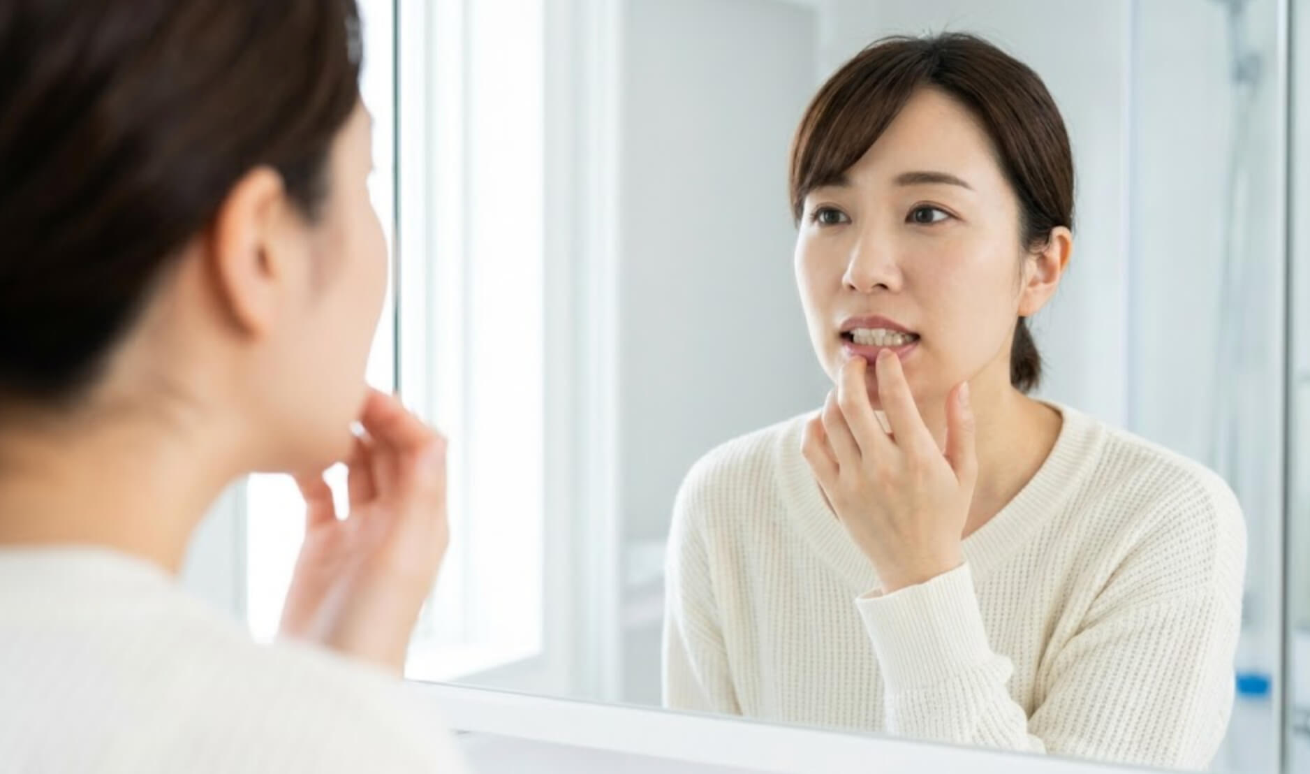 鏡の前で自分の歯並びを気にする日本人女性の様子