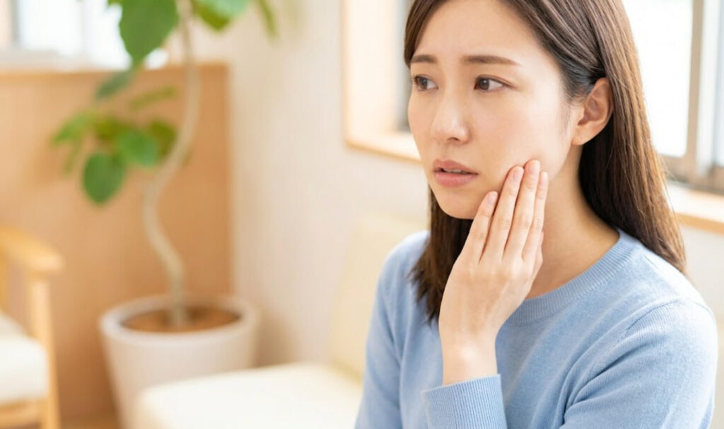 歯科医院の待合室で、口元を気にしながら不安げな表情で座る日本人女性の様子