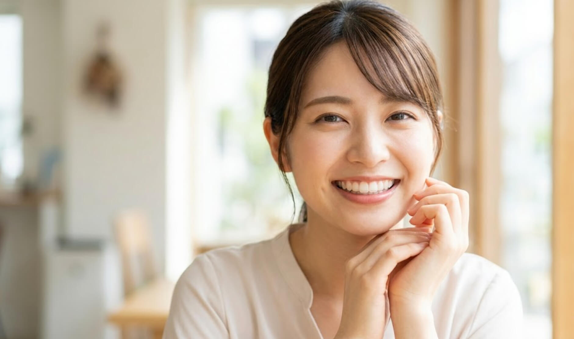 指を顎に添えて、白く整った歯並びを見せながら明るく微笑む女性の様子