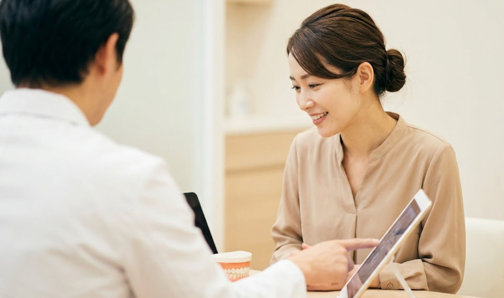 歯科医院のカウンセリングルームで、医師の説明を聞きながら安心したように微笑む日本人女性の様子