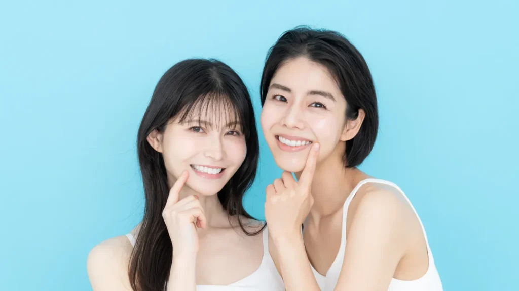 水色の背景で笑顔の口元を指さすミドル世代の女性2人（リグロスの治療を受けられる医院を解説する記事）